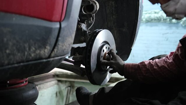 Сar mechanic replaces an old brake disc with a new one in a car repair service