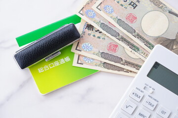 テーブルの上に置かれた銀行の預金通帳と印鑑、1万円札、電卓
