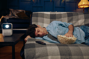 Young man with popcorn sleeping on sofa