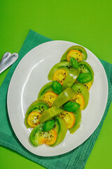 Fresh summer salad from green heirloom tomato Kiwi, fresh basil leaves and extra virgin olive oil