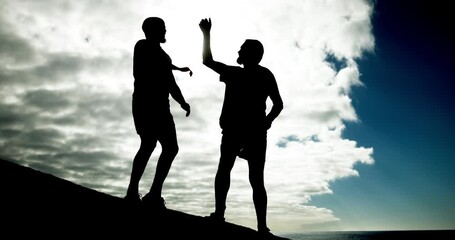 People, high five and fitness on rock at beach for helping hand, clouds and outdoor together. Men, support and lift for partnership, silhouette or low angle in training, exercise or workout in summer