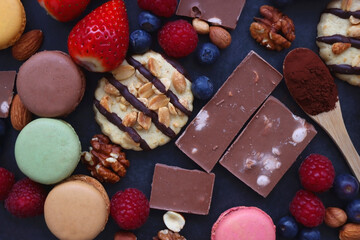 Macarons, chocolate, cookies, berries and various nuts on dark blue background. Top view.