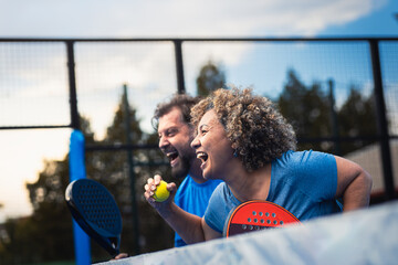 Mixed adult couple celebrate winning the point in padel on outdoor court.
