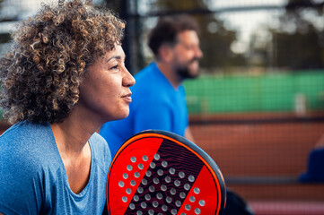 Side view portrait of mixed adult couple palying padel on outdoor court.