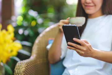 Closeup image of a woman using mobile phone and drinking coffee in the outdoors cafe