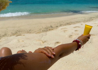 Woman hand with sunscreen cream on the sand beach as applying moisturizing lotion on .Skin care protection concept.