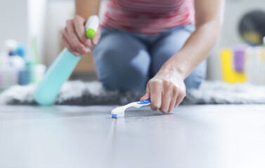 Woman cleaning the bathroom floor using a toothbrush