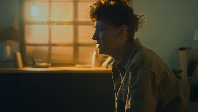 Side medium footage of depressed young man crying in despair sitting in dark room in solitude