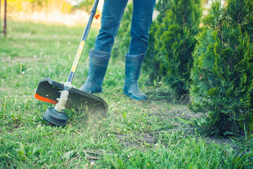 worker mows green grass on the lawn with hand trimmer. lawn care. weed control. Woman with gasoline...