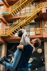 Man lifting his female couple into the air as they both smile and enjoy a moment of happiness together. The urban backdrop features and industrial staircases.