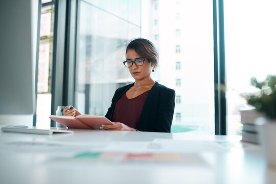 Serious, woman and office with writing on journal for business agenda, notes and information in table. Female person, employee and planning as graphic designer for creativity, ideas and vision
