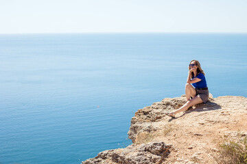 Young woman tourist enjoying a beautiful view of the sea while sitting on a rock, copy space.