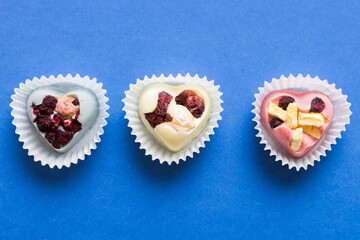 chocolate sweets in the form of a heart with fruits and nuts on a colored background. top view with space for text, holiday concept