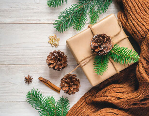 Fototapeta premium Christmas or New Year composition. Christmas gift, pine cones, cinnamon sticks, anise stars, scarf on white wooden background. Flat lay, top view, copy space