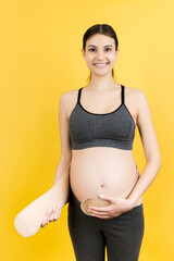 Portrait of pregnant woman putting on a bandage at yellow background with copy space. Orthopedic...