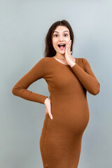 Happy pregnant woman touching her abdomen at Colored background. Future mother is wearing white...