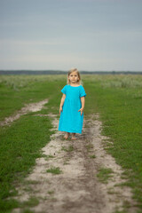 Little happy beautiful blonde girl in a blue linen sundress against the background of a green meadow, live emotions, smile. sunny day