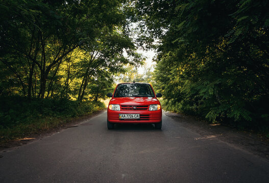 Kei car Daihatsu Mira L700 on a road in deciduous forest. Frontal view of small red car driving through the woods. Kyiv region, Ukraine - June 29 2014.
