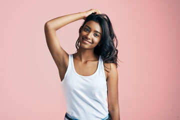 Fototapeta premium Portrait, smile and Indian girl in studio for hair care, skincare and casual fashion on pink background. Smooth skin, happy and female person with salon treatment for wavy style, keratin and volume