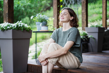 Young happy smiling Caucasian woman sitting on the wooden terrace of a country house enjoying the summer