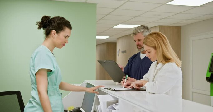 Group of medical staff at a hospital reception desk collaborating and reviewing patient records. Healthcare professionals in a clinical setting. Medical Staff Working At Hospital Reception Desk