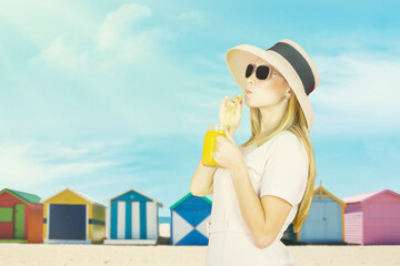 Young woman drinking fresh juice and wearing sunglasses and hat