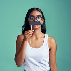 Woman, studio and party prop on face, surprised and comic with hand holding mask for humorous or...