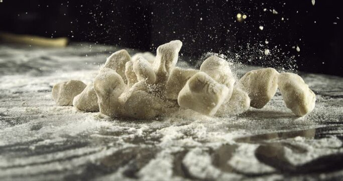 Super slow motion macro of homemade traditional recipe fresh pasta gnocchi is falling with flour dust splashes on rustic wooden table in traditional bakery kitchen at 1000 fps.