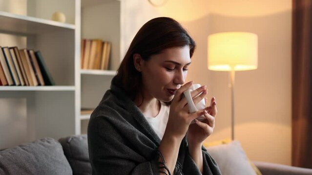Portrait of charming young brunette woman sitting on couch take sip drinking hot tea or coffee at cozy home Calm relaxed female enjoying weekend leisure time alone in the living room indoors