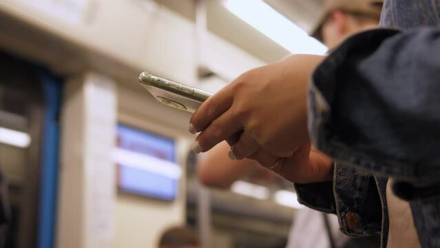Hands of a woman using a smartphone in a crowded train car in the subway close-up. A girl in the subway searches for information on the Internet, reads, studies online or sends text messages.