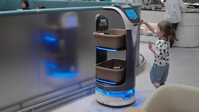 Little Girl Toddler Puts Used Cup in Basket of Robot Collecting Dirty Dishes at Martina Lounge, Incheon Airport