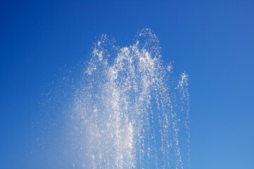 Liquid spraying from fountain against electric blue sky in natural landscape