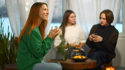 Students talk and relax in cozy cafe. Media. Beautiful young woman is drinking tea on background of talking couple. Students relax and drink tea in college cafe