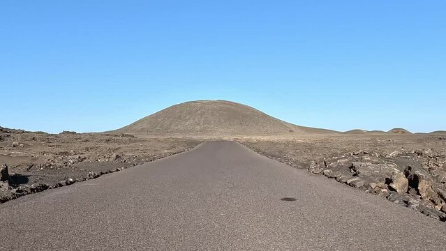 Vehicle view driving over Lanzarote Parque Nacional de Timanfaya national park showing the rough landscape left and right of the road of the volcanic rock and mountain in background 4k resolution