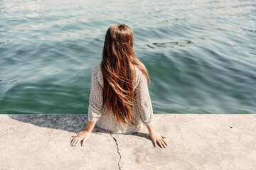 A woman is sitting on a ledge by a body of water, wearing a dress with a leopard print pattern. The scene is peaceful and serene, with the woman enjoying the view of the water and the surrounding area