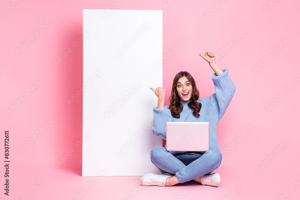 Poster full length photo of excited cheerful person sit floor use netbook direct fingers empty space billbo