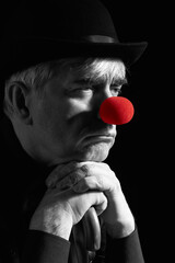 Dramatic selective color portrait of a clown against a dark background leaning on the handle of an...