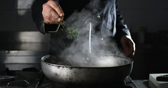Super slow motion close up of professional chef put cut parsley leaves traditional Italian dish of spaghetti with red tomato sauce on pan to be cooked in kitchen of restaurant.