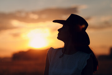 Woman farmer silhouette in cowboy hat at agricultural field on sunset