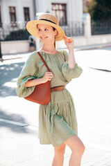 Young beautiful smiling brunette woman in trendy summer dress. Sexy carefree woman posing in street. Positive model outdoors at sunny day. Cheerful and happy. In hat. Holds handbag