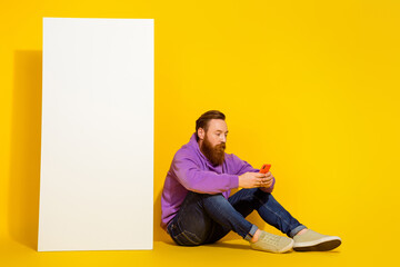Full body photo of nice person sit floor hold use telephone empty space big screen isolated on yellow color background