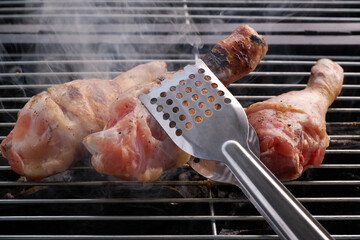 Tongues flipping chicken legs on bbq grill close-up.