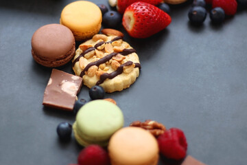 Macarons, chocolate, cookies, berries and various nuts on dark blue background. Selective focus.