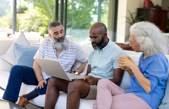 Diverse senior friends gathering around laptop at home