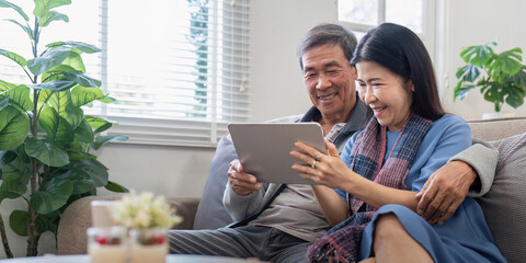 Senior couple happily using tablet at home. Concept of technology, companionship, and relaxation