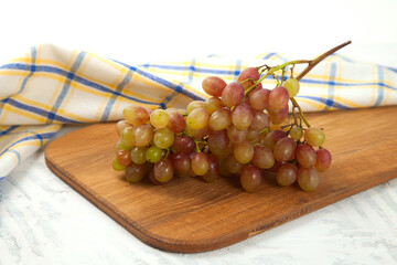 Cutting board with bunch of organic pink grapes on white wooden background..