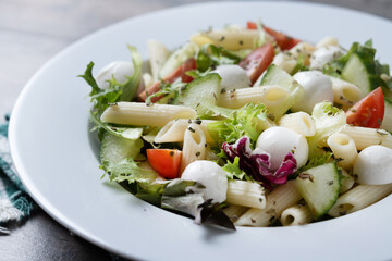Pasta salad with vegetables and mozzarella cheese on wooden table. Close up