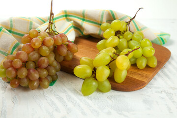Cutting board with bunch of organic green and pink grapes on white wooden background..