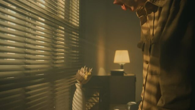 Side tilt footage of young Caucasian man tearing old photos and getting compulsive and crazy, throwing pictures from table and shouting at night indoors