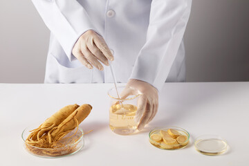 Laboratory instruments containing ginseng featured on white table top with a beaker of yellow...